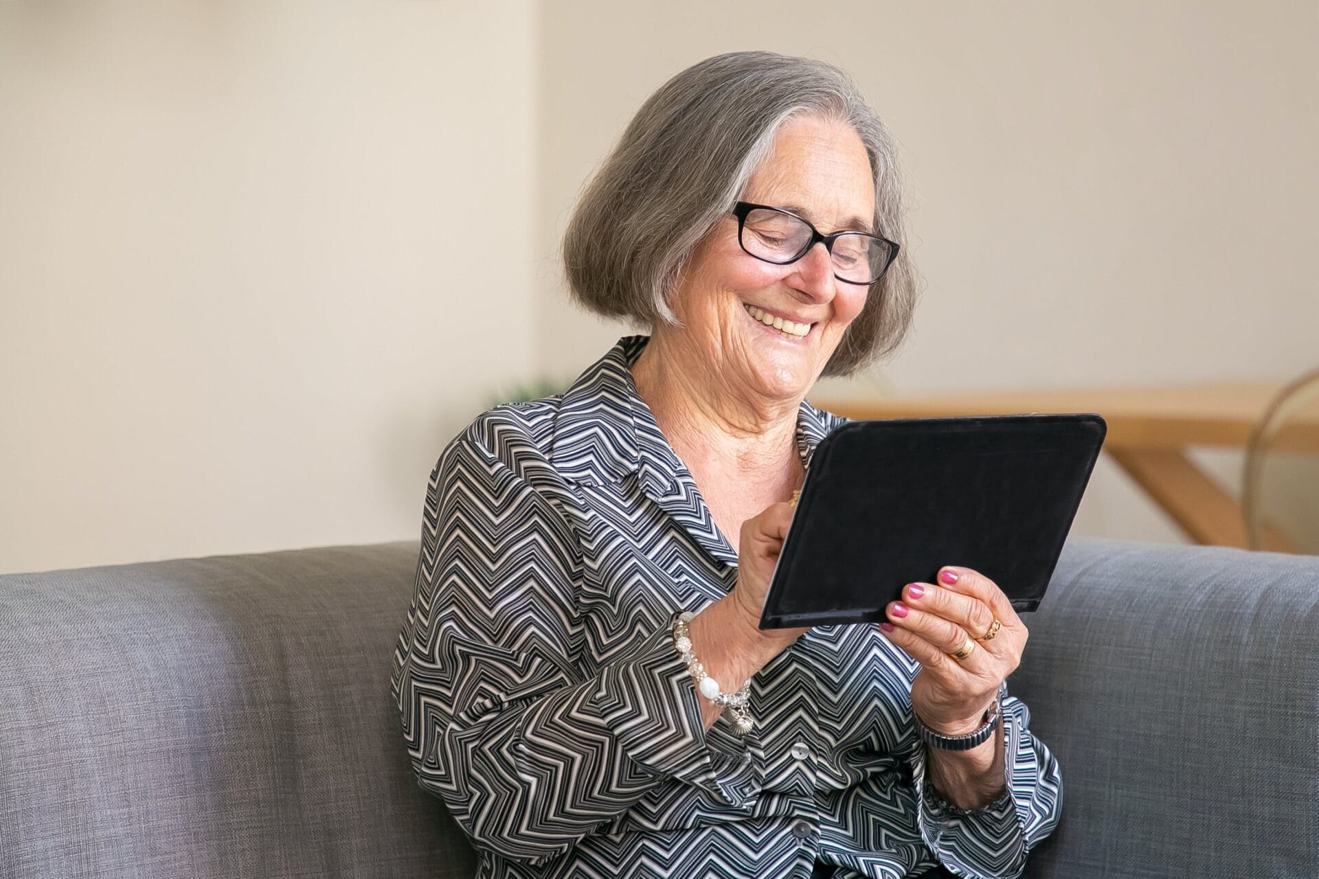 An elderly woman smiling at a mobile tablet