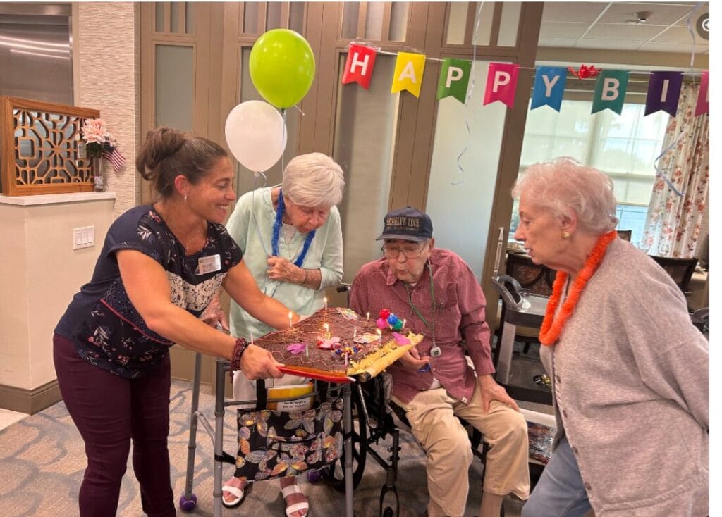 Elderly people blowing out candles on a giant cake for a birthday celebration at a long-term care facility