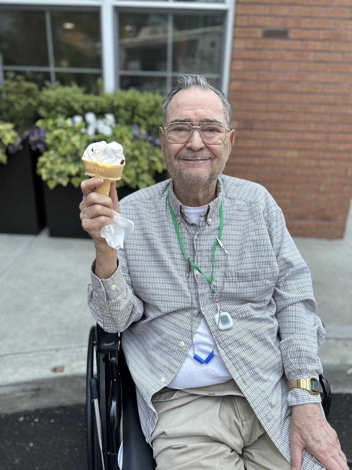 A senior in a wheelchair smiling and holding up an ice cream cone.