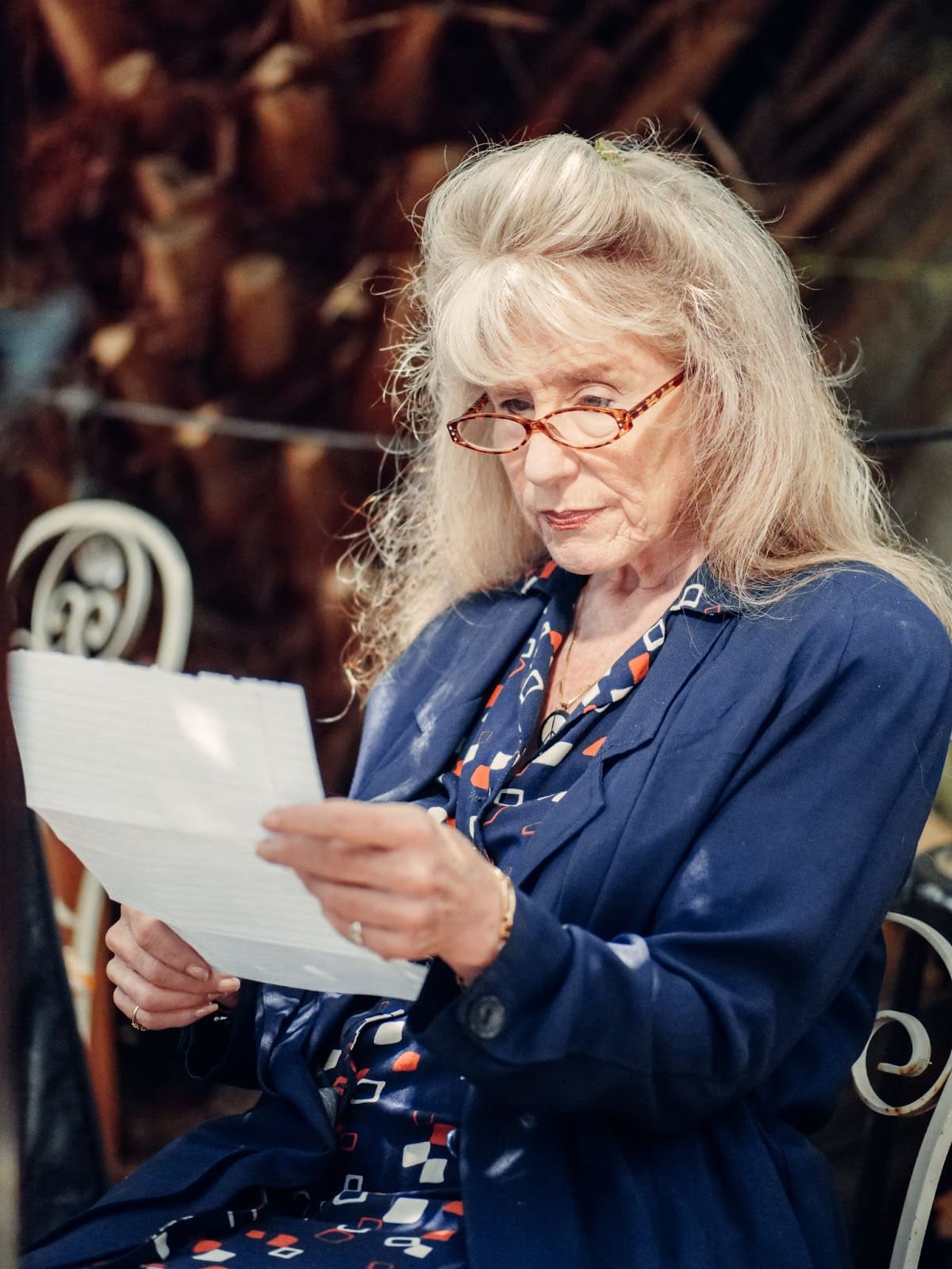 An elderly woman sitting on a bench and reading a paper statement