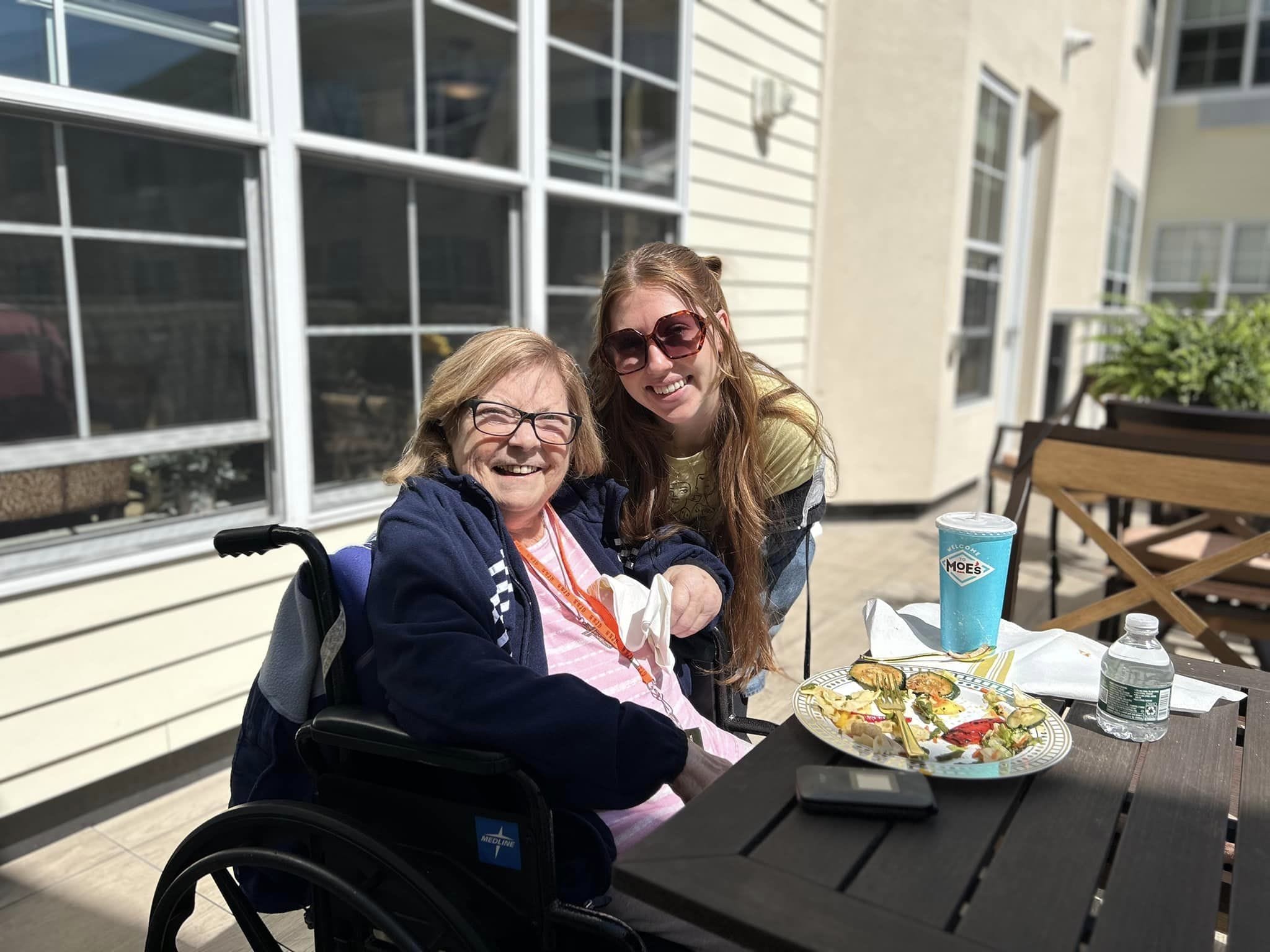 A young lady and a woman in a wheelchair smiling over a plate of food