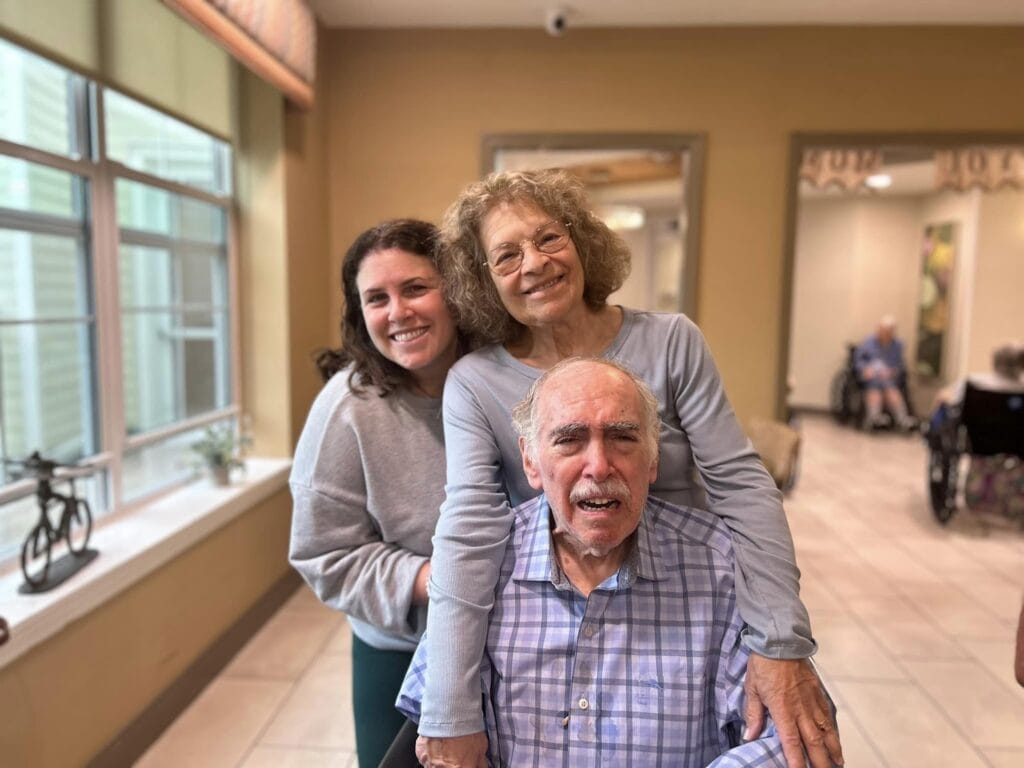 Two women standing behind a man with dementia in a wheelchair