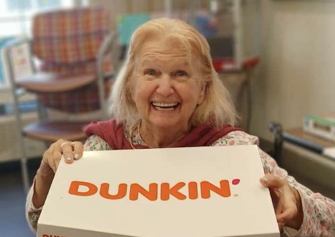 A woman with dementia smiling with a box of Dunkin Donuts