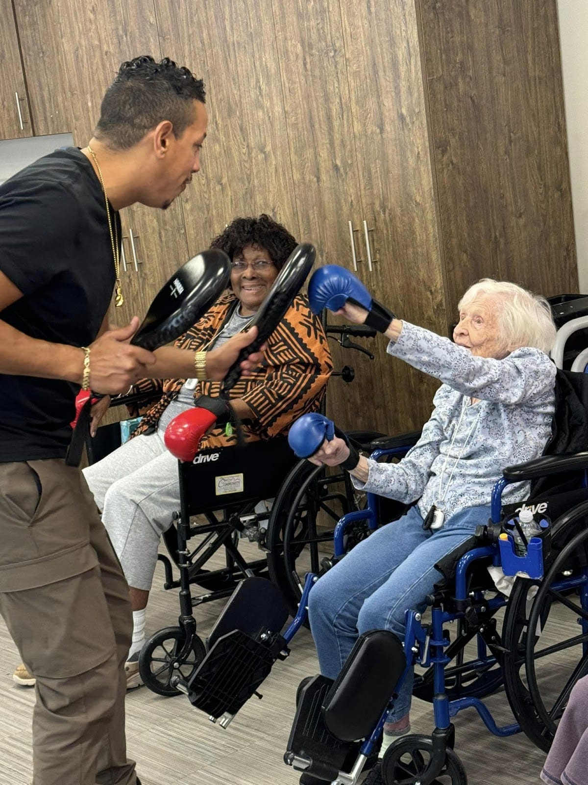 Seniors in a wheelchair with boxing gloves sparring with a boxing class teacher