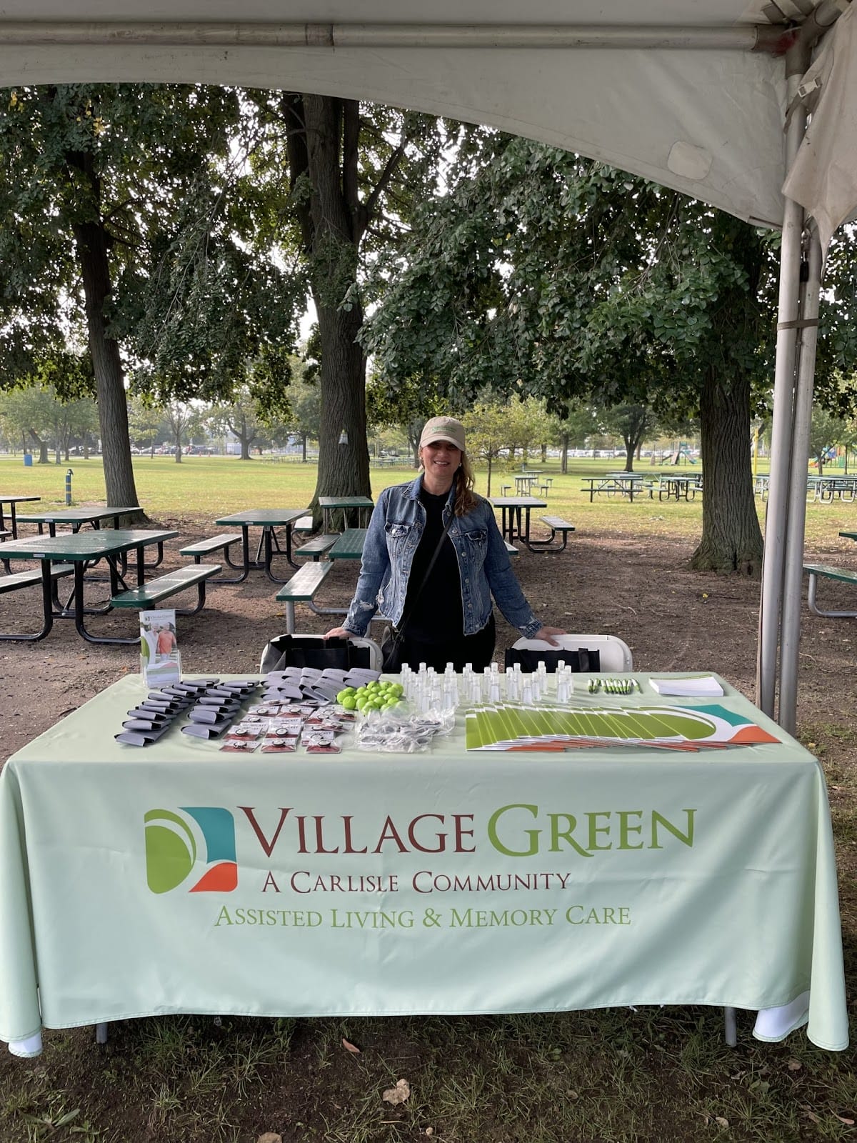 A Village Green staff member smiling at a booth full of Village Green marketing paraphernalia