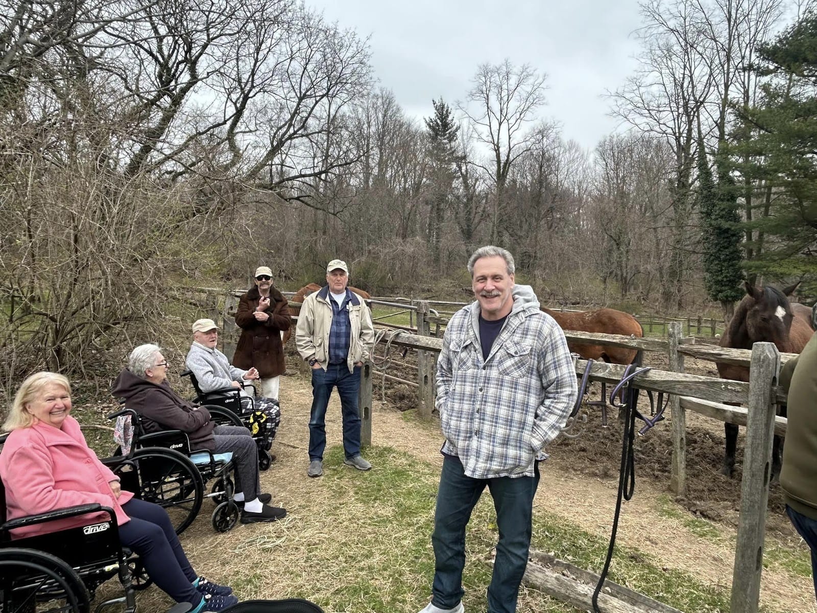 Assisted living residents in wheelchairs outdoors with horses