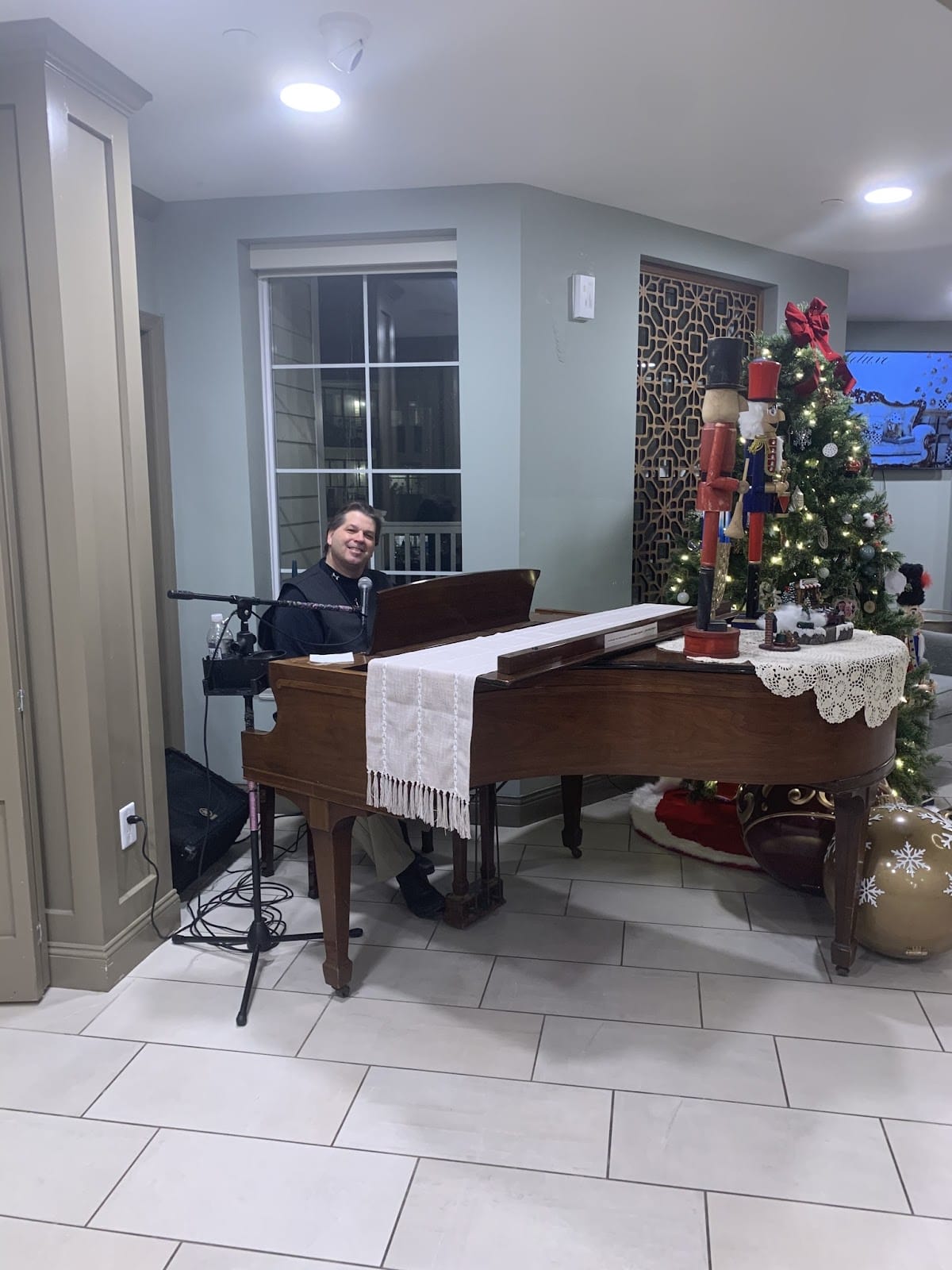 A picture of a performer sitting at a grand piano next to a Christmas tree 