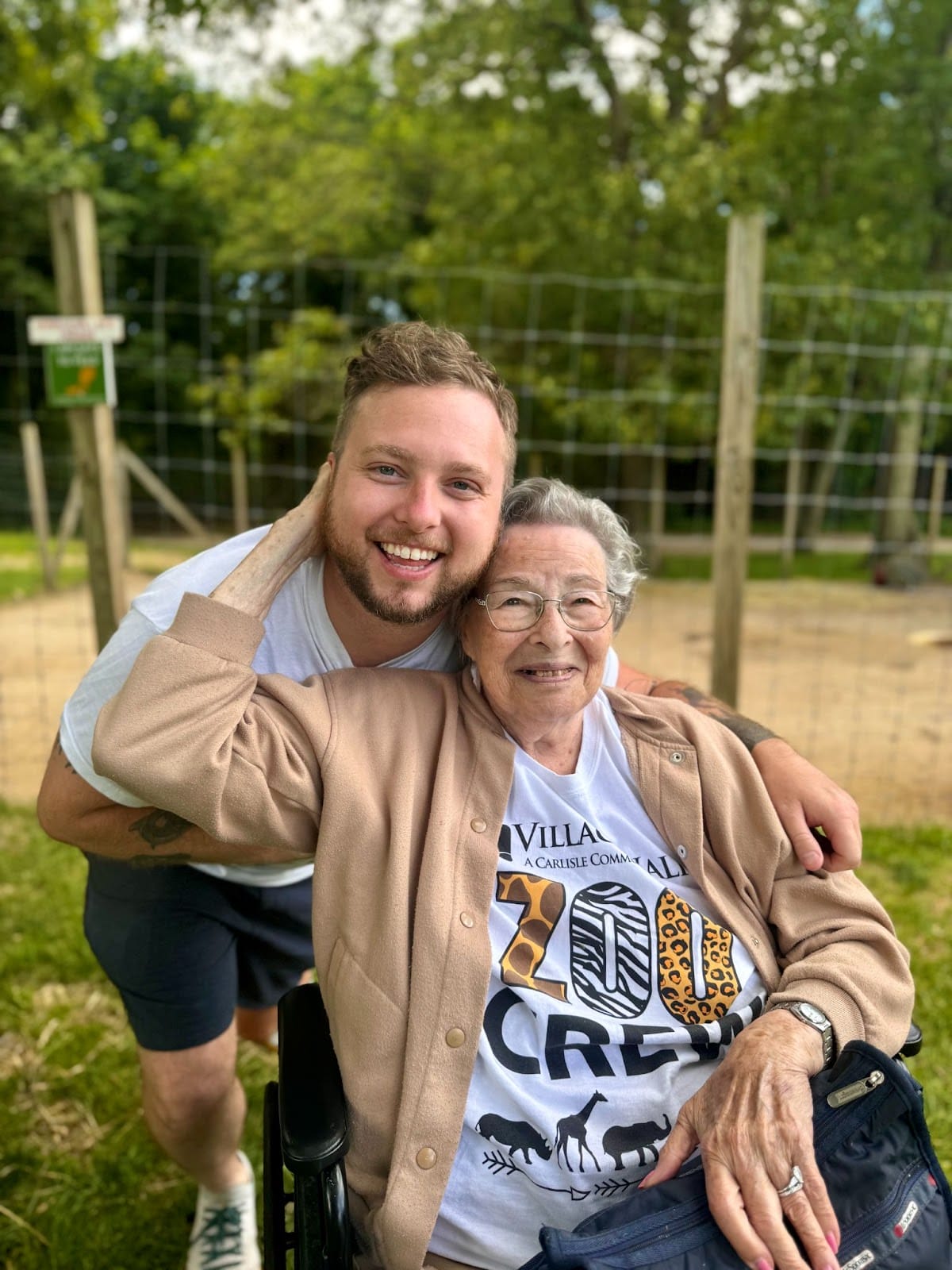 An assisted living resident with limited mobility hugging an assisted living staff member and smiling at the camera