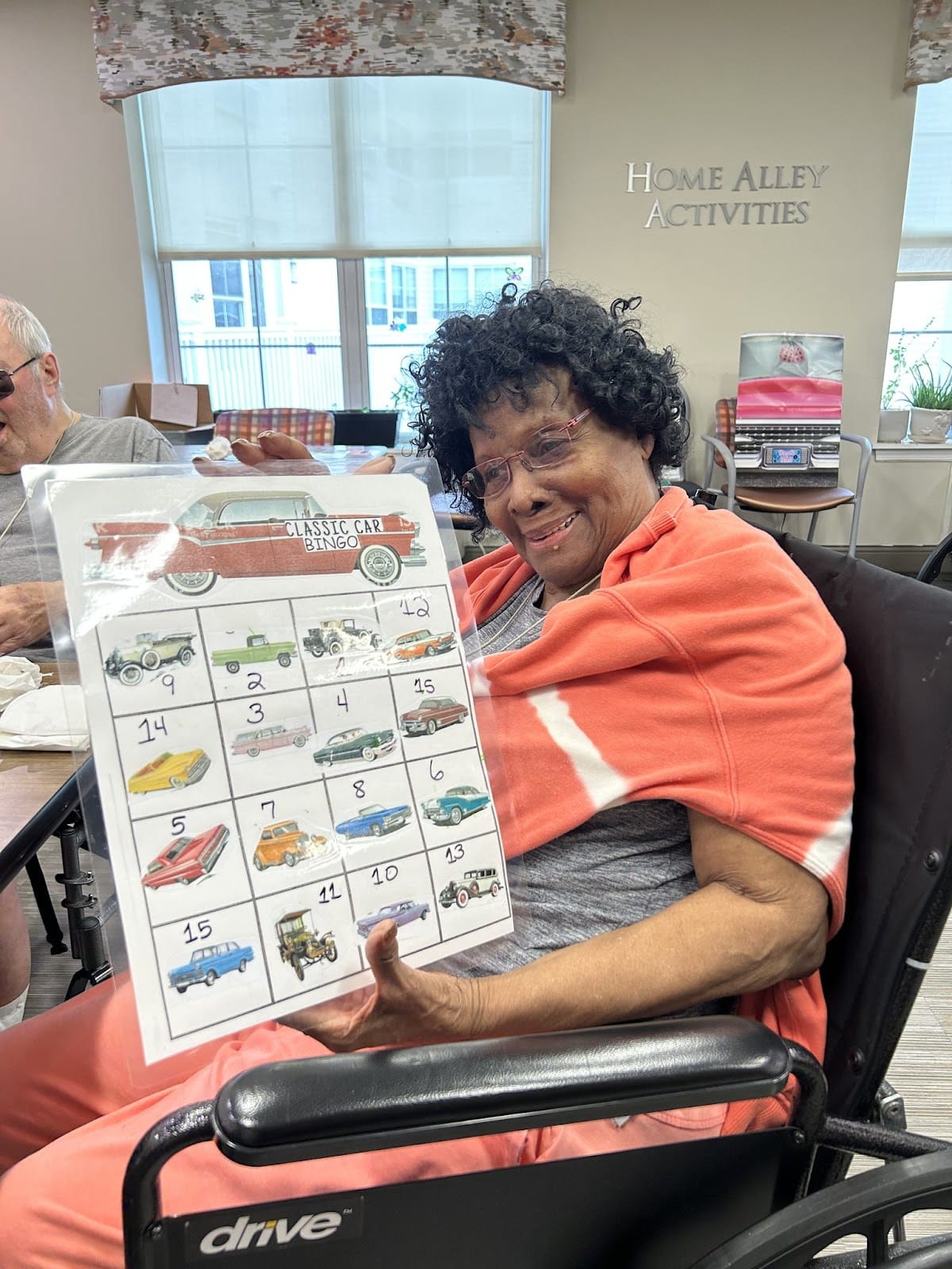 A senior with limited mobility in a wheelchair playing and holding up a Car Bingo card