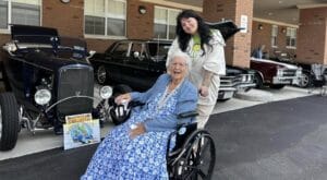 A picture of a woman smiling with a smiling assisted living resident in a wheelchair