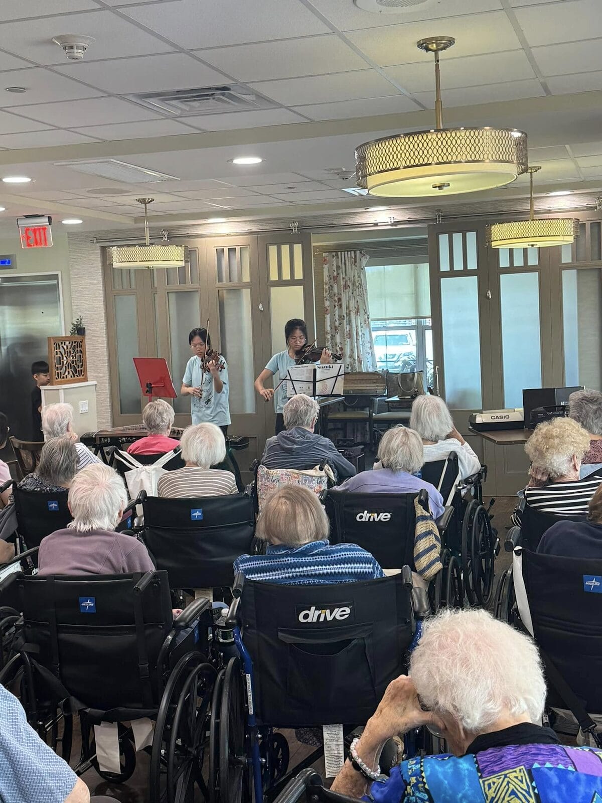 A group of student violinists playing for a group of seniors in wheelchairs at a senior living facility