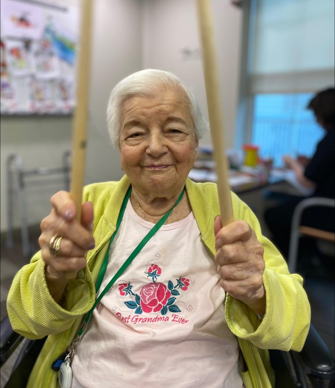 An elderly woman smiling while holding drum sticks in a music therapy session