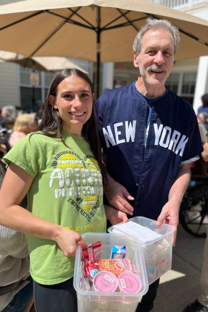 A picture of a young woman smiling with an older adult with toys in a bin in their hands