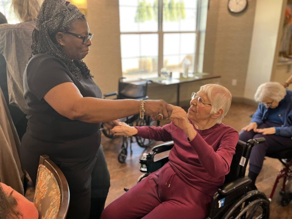 A woman with memory loss due to depression sitting in a wheelchair being danced with by a standing aid