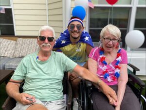 A picture of two senior citizens holding hands with a dementia caregiver in the background